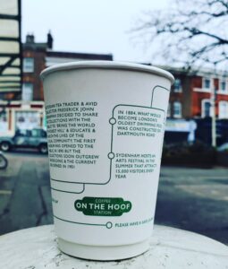 White coffee cup on an outdoor table with green text designed like a tube map.