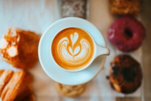 Ariel photo of an espresso coffee in a white cup and saucer with delicious looking doughnuts and pastries in the background.