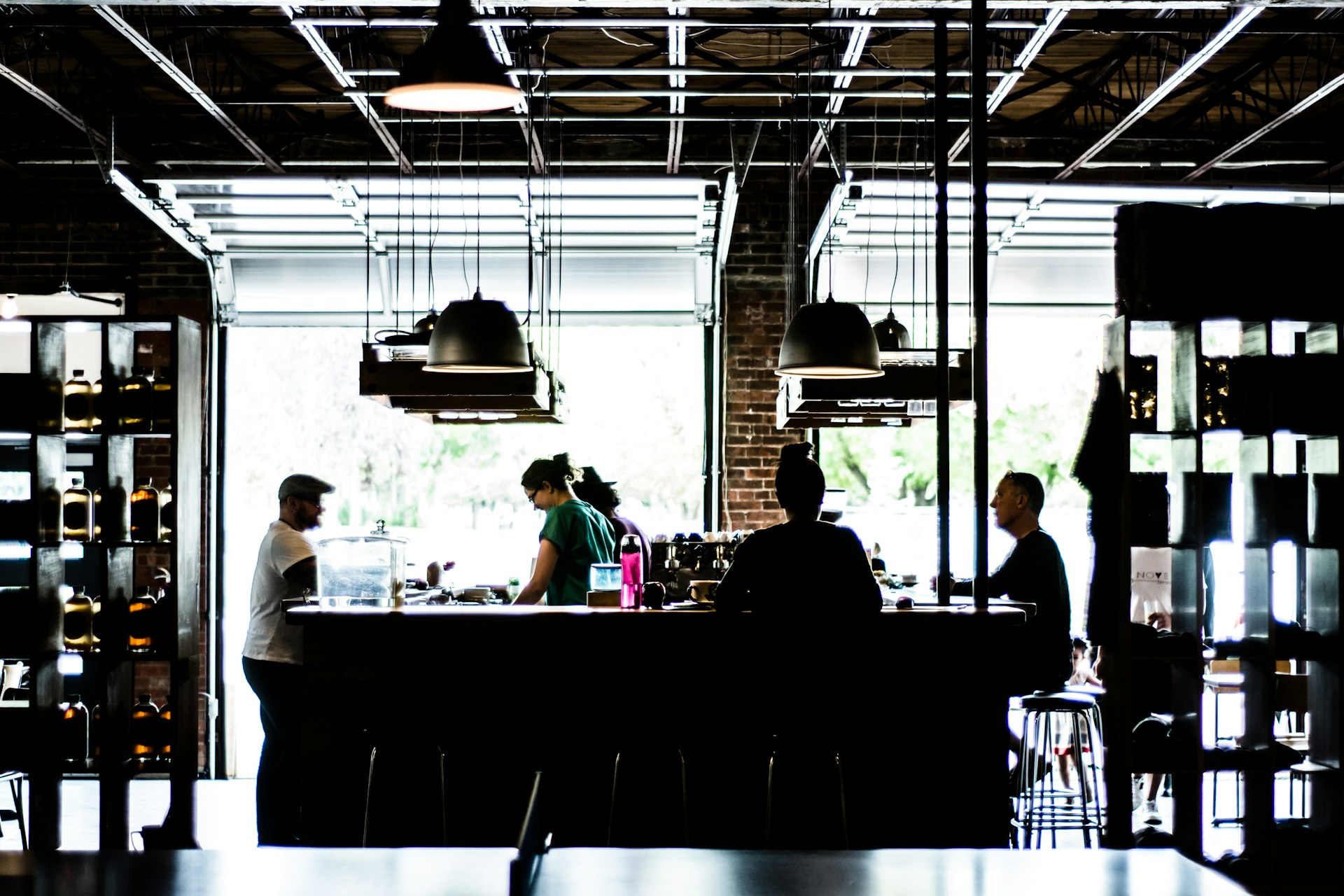 Dark photo of a spacious coffee shop with a central counter and a few people working and sitting there. There's a big window in the background.