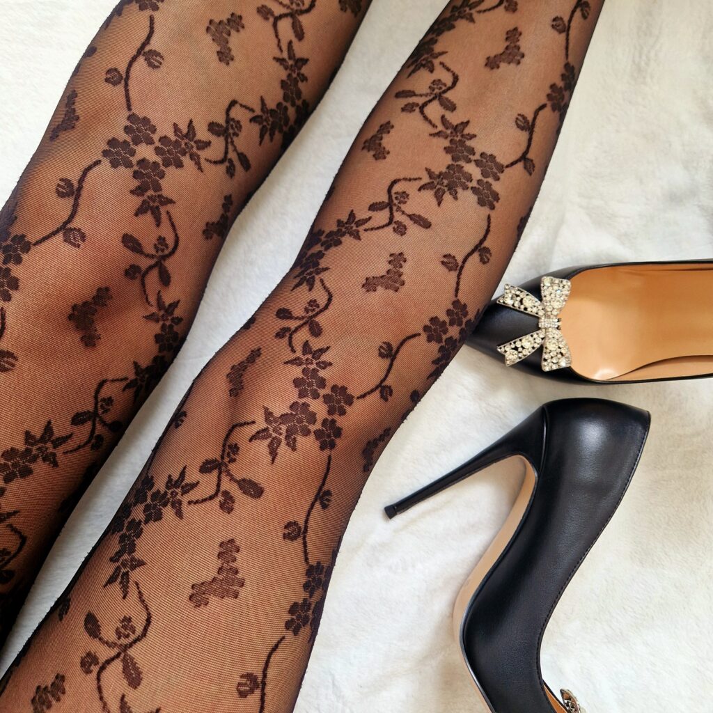 A pair of slim legs with pretty lace patterned black tights. A paid of high heels black shoes lie next to the right leg.